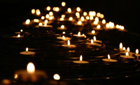 A multitude of candle flames shine against a dark background.
