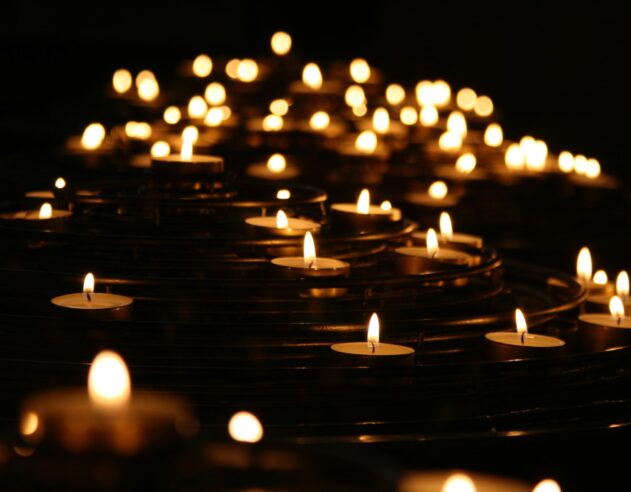 A multitude of candle flames shine against a dark background.